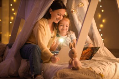 El feneriyle sevimli küçük bir kız ve annesi geceleri kulübede hikaye okuyor.