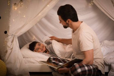 Baba, küçük oğluna masal okuyor. Kulübede yatıyor.