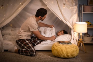 Baba, uyuyan oğlunu evinde battaniyeyle örtüyor.