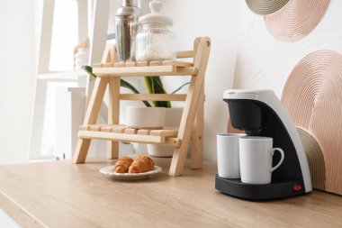 Mutfak masasında fincanları, şekeri ve kruvasanı olan modern kahve makinesi.