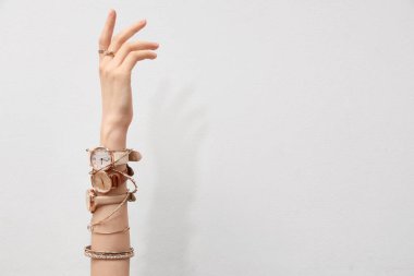 Beyaz arka planda altın kol saatleri ve bilezikleri olan bir kadın.