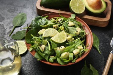 Bir kase lezzetli avokado salatası, ıspanak yaprakları ve siyah arka planda limon.