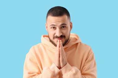 Apologetic young man on blue background, closeup clipart