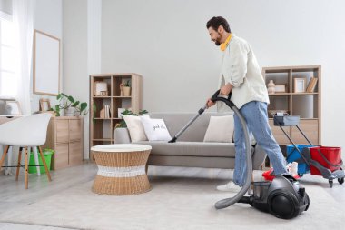 Yakışıklı adam evdeki elektrikli süpürge kanepesini temizliyor.