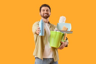 Sarı arka planda bir kova temizlik malzemesi olan yakışıklı bir adam.