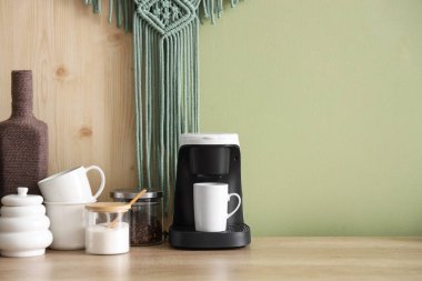 Mutfaktaki yeşil duvarın yanında fincanlı kahve makinesi ve şeker.