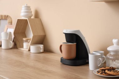 Bej duvarın yanında fincanlı kahve makinesi.