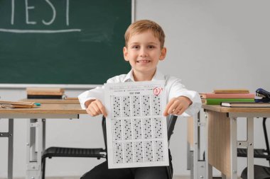 Sınav sonuçlarıyla sınıfta oturan tatlı bir okul çocuğu.