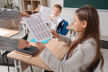 Sınıfta öğretmenden not alarak cevap kağıdı alan tatlı bir kız.