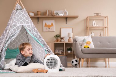 Evdeki elektrikli vantilatör ısıtıcısının yanındaki çadırda yatan sevimli küçük çocuk.