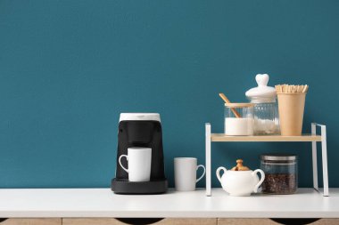 Kahve makinesi, fincanlar ve şeker mavi duvarın yanında.