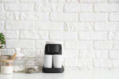 Bardaklı kahve makinesi ve beyaz tuğla duvarın yanındaki rafta şeker.