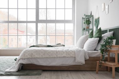 Yatak odasının içinde büyük yatak odası, raf ünitesi ve ev bitkileri var.