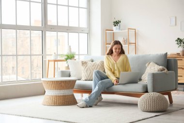 oturma odasında kanepede otururken dizüstü kullanarak güzel bir genç kadın