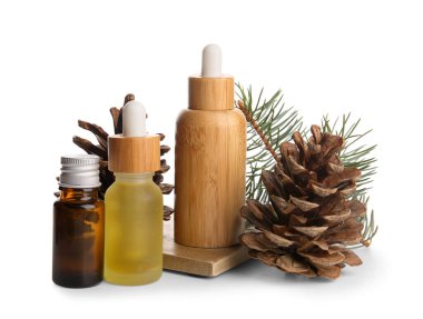 Beyaz zemin üzerinde çam kozalakları ve köknar dalı olan gerekli yağ şişeleri