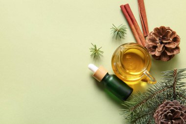 Çam kozalaklı bir şişe yağ, köknar dalları ve yeşil arka planda tarçın.