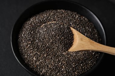 Siyah arka planda chia tohumları olan bir kase ve tahta kaşık.