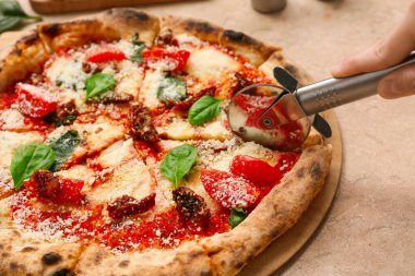 Kadın eli bej arka planda Margarita pizzası kesiyor. Yakın çekim.