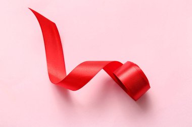 Pembe arka planda yuvarlanmış kırmızı kurdele