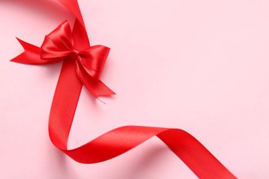 Pembe arka planda fiyonklu güzel kırmızı kurdele, yakın plan.