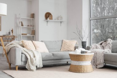 Masanın üzerinde gri kanepeler ve Noel dallarıyla aydınlık oturma odasının içinde.