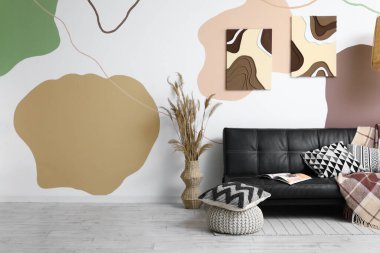 Rahat bir kanepe, yastıklı bir puf ve odanın renkli duvarlarında resimler.