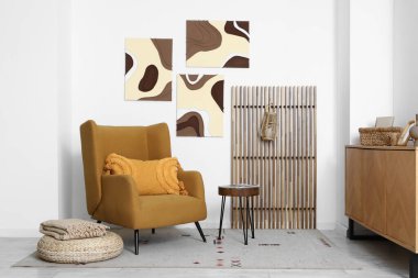 Koltuk, çekmeceler ve beyaz duvardaki tablolar.