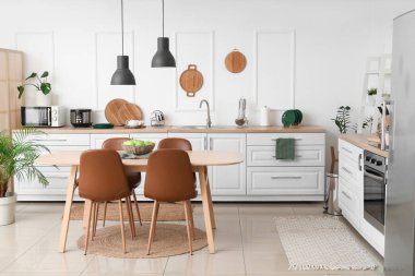 Mutfağın içinde beyaz tezgahlar, yemek masası ve lambalar var.