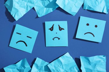 Mavi arka planda üzgün yüzler çizilmiş kağıt kağıtlar