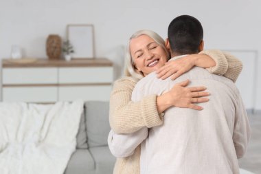 Olgun bir kadın, evinde oğluna sarılıyor.