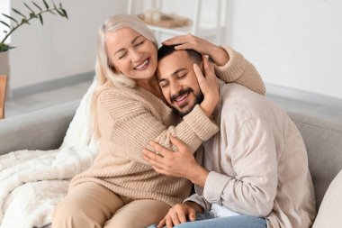 Olgun bir kadın evdeki kanepede oğluna sarılıyor.