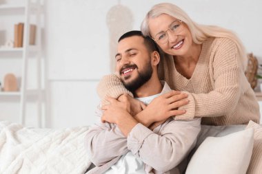 Olgun bir kadın evdeki kanepede oğluna sarılıyor.