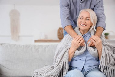 Evdeki kanepede annesini sıcak ekoseyle örten genç bir adam.