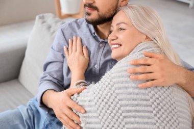 Genç adam evde ekoseyle annesine sarılıyor, yakın plan.