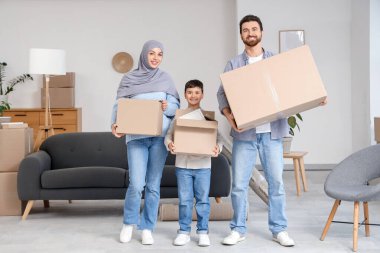 Happy Muslim family with cardboard boxes in room on moving day clipart