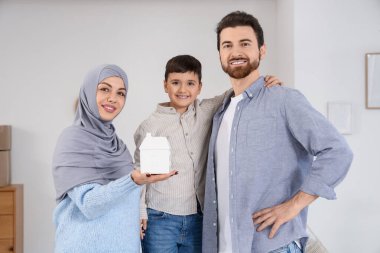 Happy Muslim family with house model in room on moving day clipart