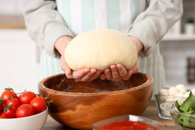 Mutfaktaki ahşap masanın yanında çiğ hamurlu ve pizza malzemeli bir kadın.