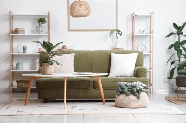 Oturma odasının içinde yeşil kanepe, kahve masası ve bitkiler var.