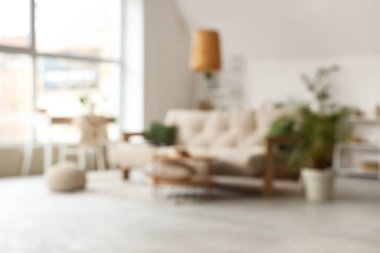 Oturma odası, bej kanepe, sehpa ve bitkilerle bulanık görünüyor.