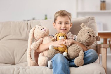 Evdeki kanepede oturan örülü oyuncaklarla sevimli küçük çocuk.