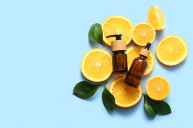 Portakal yağı şişeleri ve mavi arka planda taze meyve dilimleri.