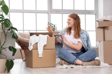 Evde yeni kıyafetlerle paket kutularını açan genç bir kadın var.