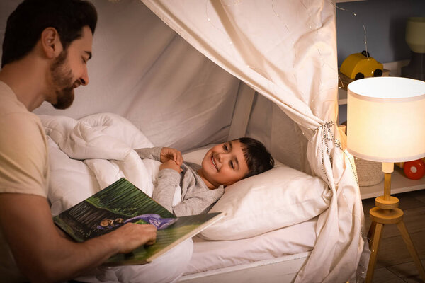 Милый мальчик слушает отца, читающего сказку на ночь в хижине дома.