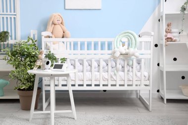 Yatak odasının içinde beşik, raf üniteleri ve bebek monitörü var.