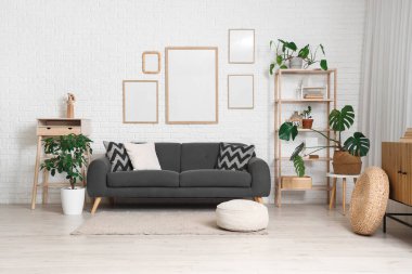 Rahat bir kanepe, raflar ve beyaz tuğlalı duvarda boş posterler.