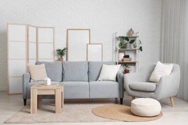 Konforlu kanepe, koltuk, sehpa ve oturma odasındaki beyaz tuğla duvarın yanındaki boş posterler.