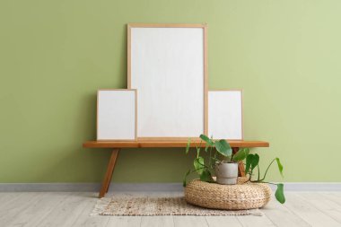 Bankta boş posterler ve oturma odasındaki yeşil duvarın yanında çiçek var.