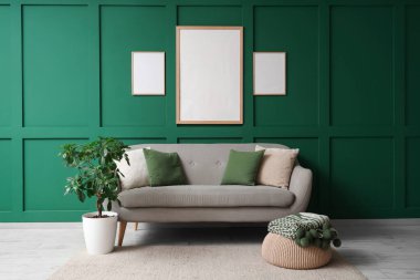 Konforlu kanepe, çiçek ve yeşil duvarda boş posterler.