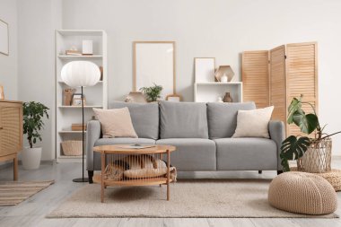 Gri kanepe, lamba ve bitkilerle aydınlık oturma odasının içinde.