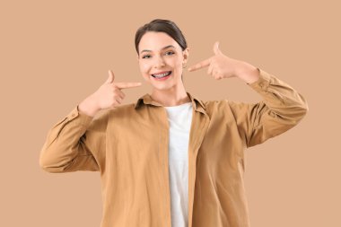 Gülümseyen genç kadın bej arka plandaki diş tellerine işaret ediyor.